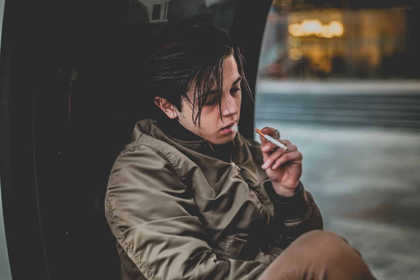 man wearing gray jacket holding cigarette